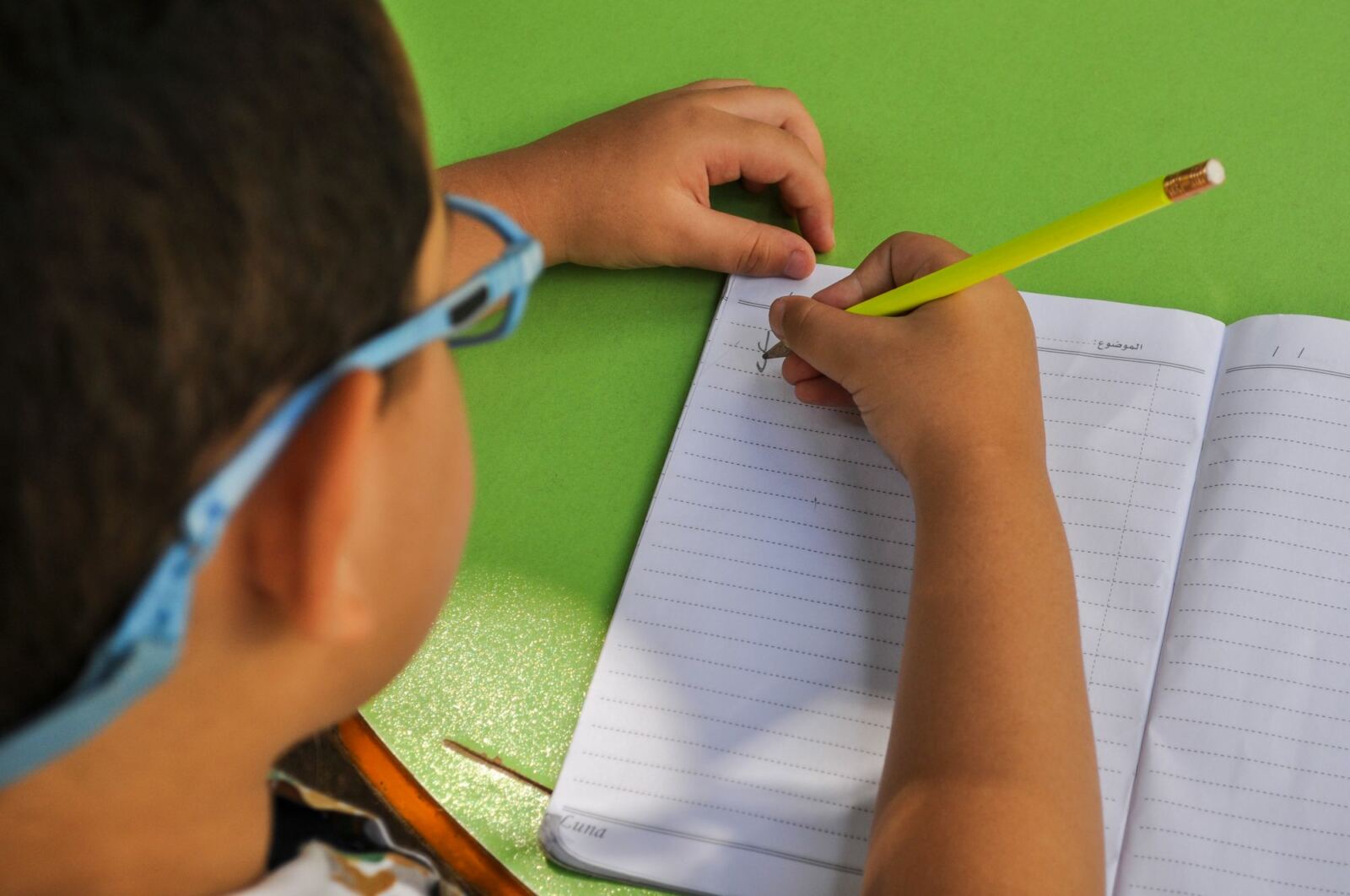 Enfant à lunettes écrivant au crayon dans un cahier ligné