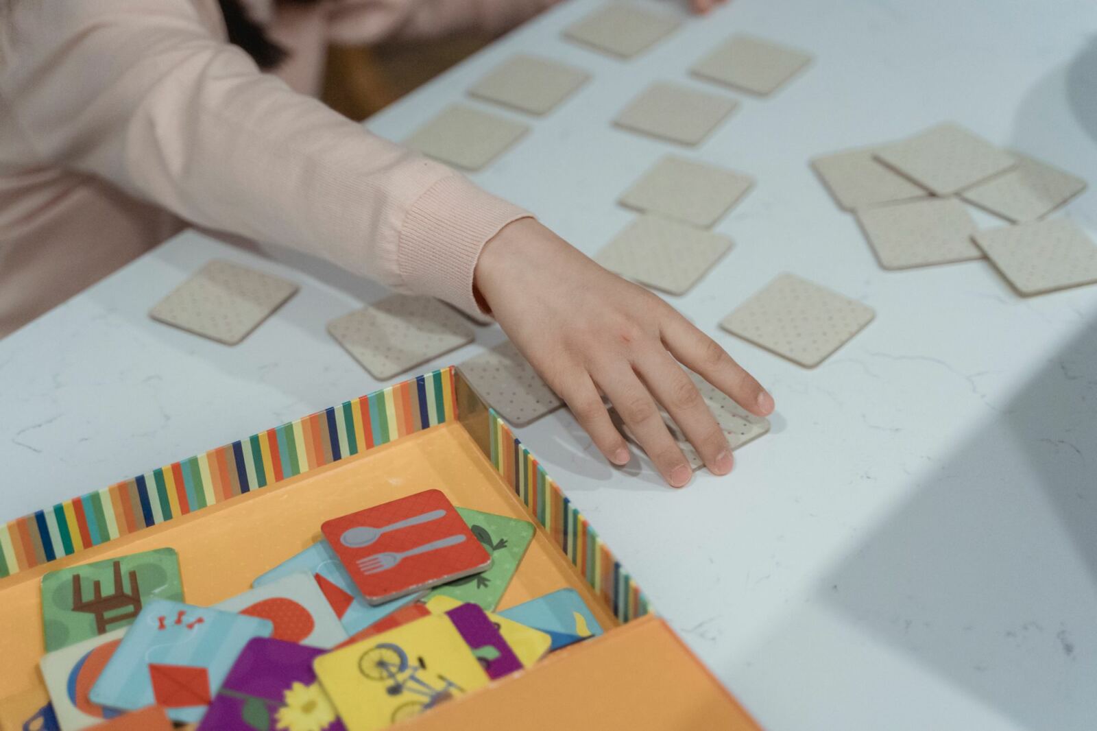 Mains d'un enfant qui retournent des cartes d'un jeu de mémoire posé sur une table